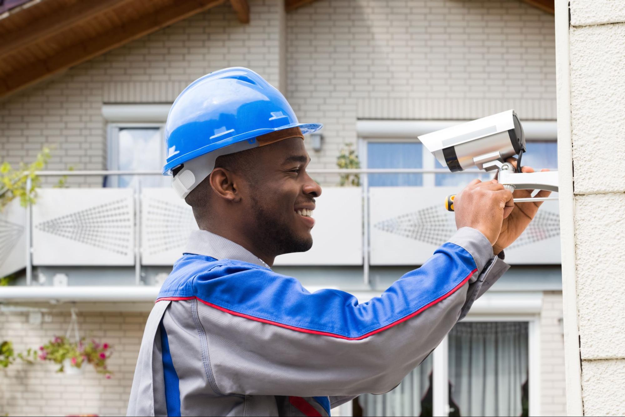 Man in blue helmet installing security camera on building