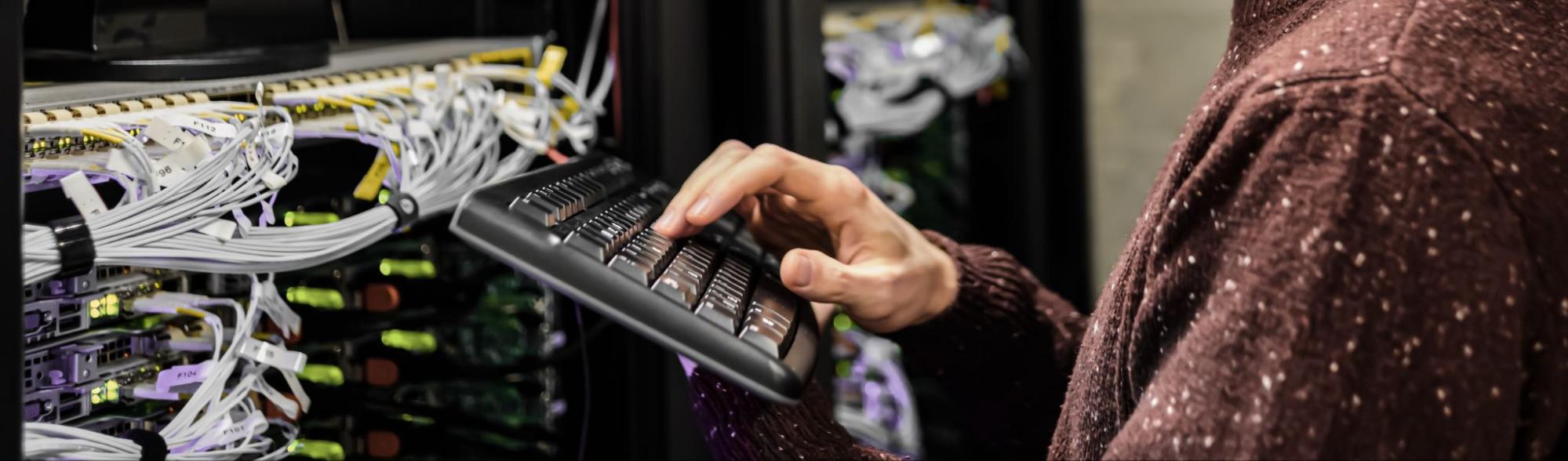 Close up of person's hand typing on keyboard in front of server