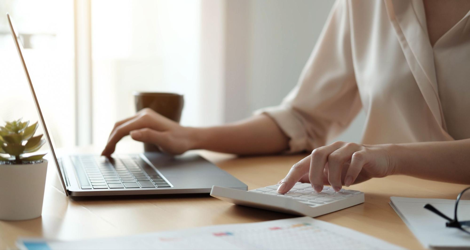 Person with face not shown working with laptop and calculator