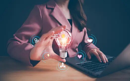 A woman working on her laptop and holding a lightbulb, with surrounding holographic icons.