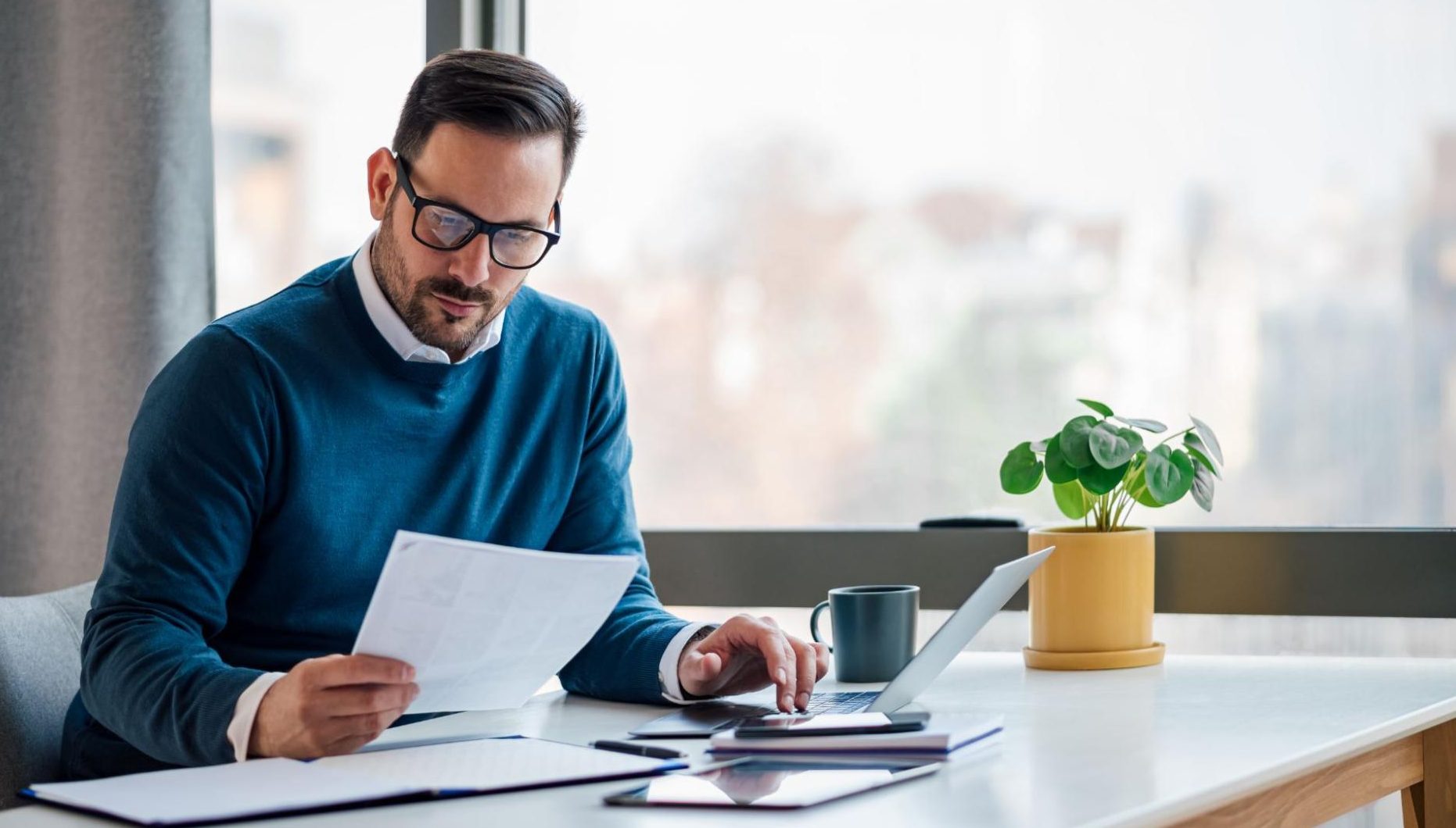 Man in teal sweater looking at paper at desk