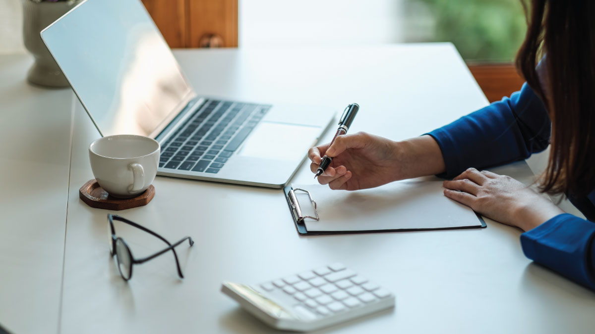 woman taking notes while using computer and calculator